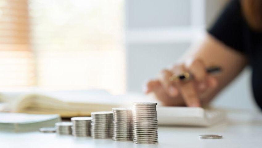 Piles de pièces de monnaie en gros plan avec une personne floue utilisant une calculatrice à l'arrière-plan, représentant des concepts de finance, d'épargne ou de comptabilité.